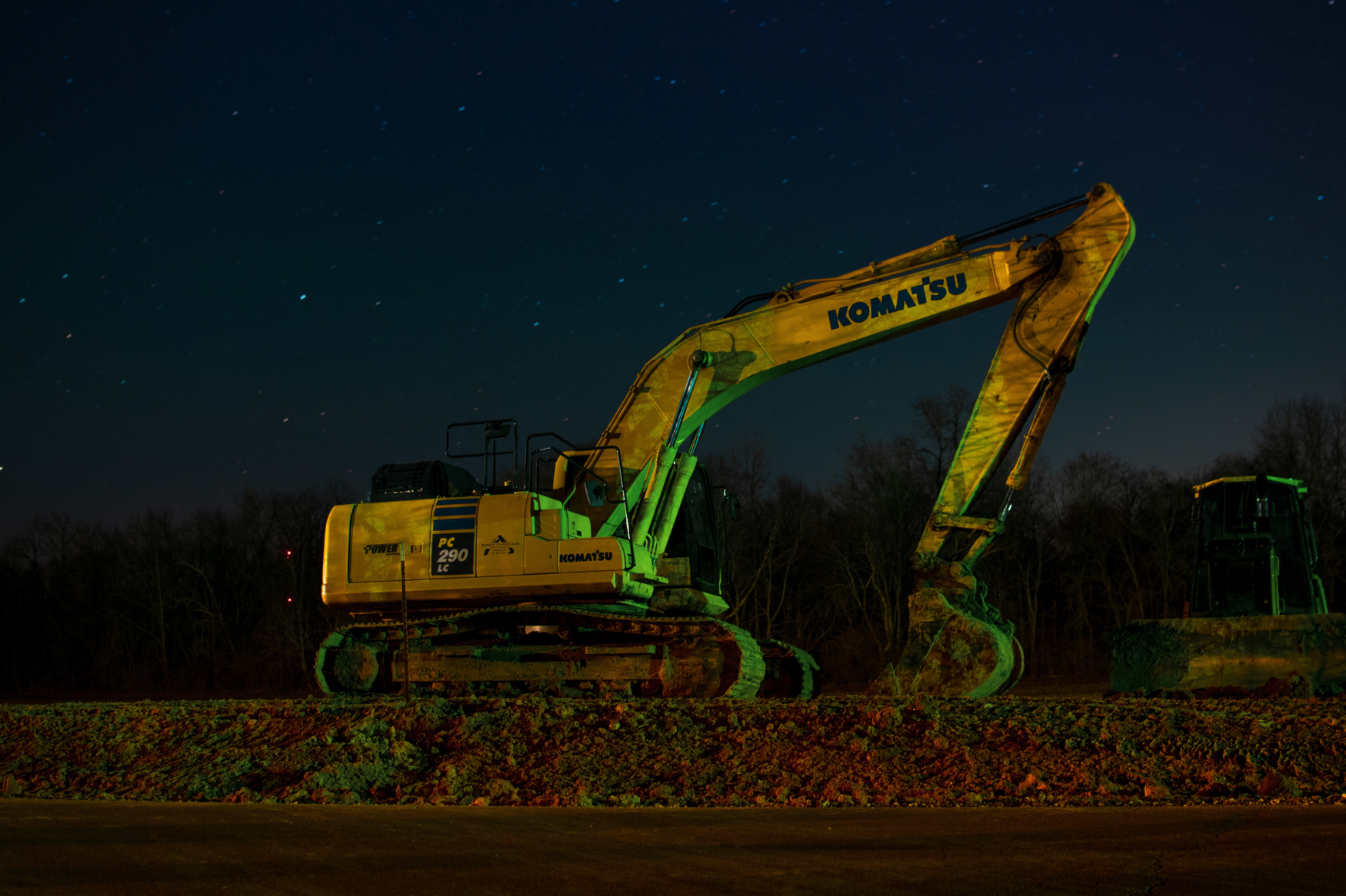 Komatsu excavator working a land-clearing job at night under floodlights